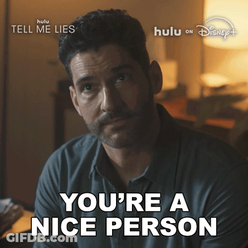 A Man With A Beard Says " You 'Re A Nice Person " In Front Of A Poster For Tell Me Lies GIF