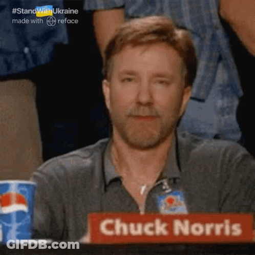 A Man With A Beard Sits At A Table With A Sign That Says Chuck Norris GIF