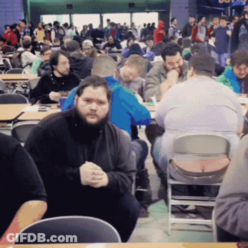 A Man With A Beard Sits In A Crowded Restaurant GIF