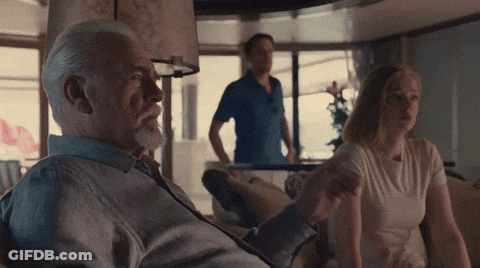 A Man With A Beard Sits On A Couch With A Woman And A Man Standing Behind Him GIF