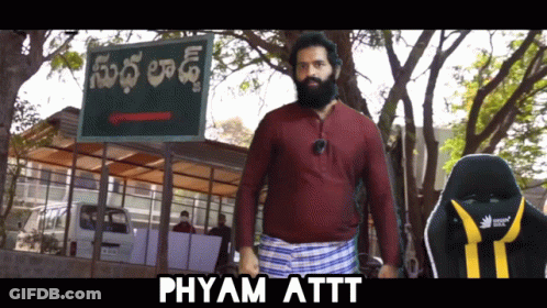 A Man With A Beard Standing In Front Of A Sign That Says Phyam Attt GIF