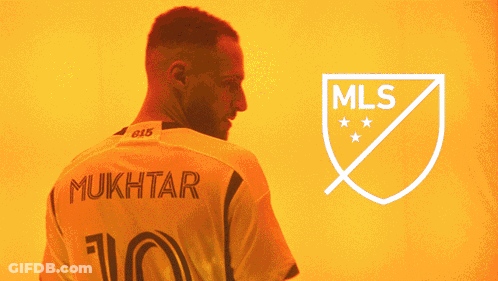 A Man With A Beard Stands In Front Of A Logo For The Mls GIF