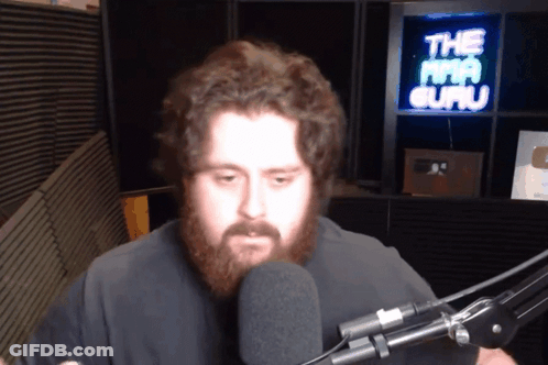 A Man With A Beard Stands In Front Of A Microphone In Front Of A Sign That Says The Mma Guru GIF
