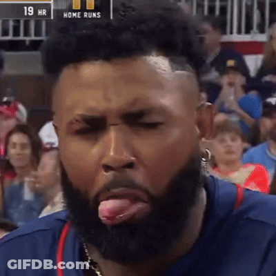 A Man With A Beard Sticking His Tongue Out In Front Of A Scoreboard That Says Home Runs GIF