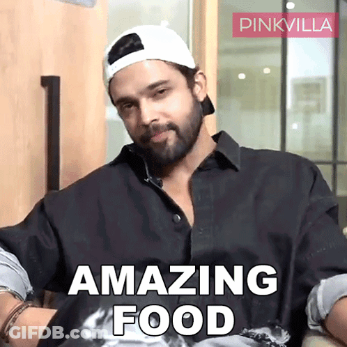 A Man With A Beard Wearing A Baseball Cap And A Black Shirt Says " Amazing Food " GIF