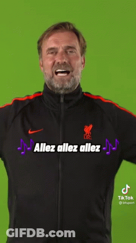 A Man With A Beard Wearing A Black And Orange Nike Jacket Is Smiling . GIF