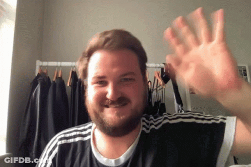 A Man With A Beard Wearing A Black And White Adidas Shirt Is Waving GIF