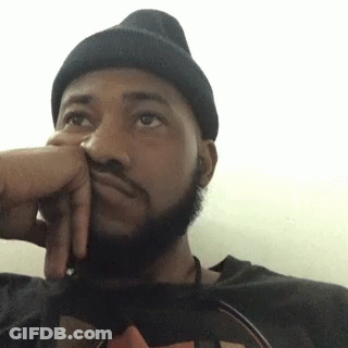 A Man With A Beard Wearing A Black Beanie Is Sitting Down With His Hand On His Face . GIF