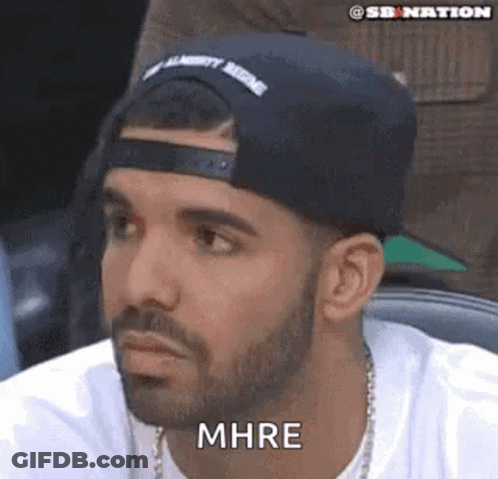 A Man With A Beard Wearing A Black Hat And A White Shirt Is Sitting In A Chair . GIF