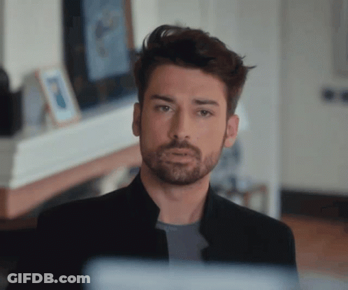 A Man With A Beard Wearing A Black Jacket Looks At The Camera GIF