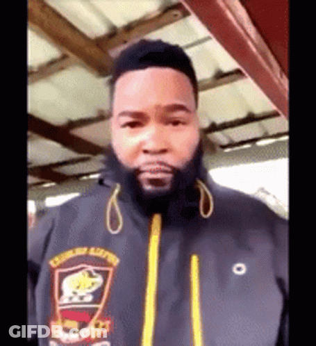 A Man With A Beard Wearing A Black Jacket With A Yellow Zipper GIF