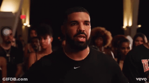A Man With A Beard Wearing A Black Nike Shirt Stands In Front Of A Crowd Of People . GIF