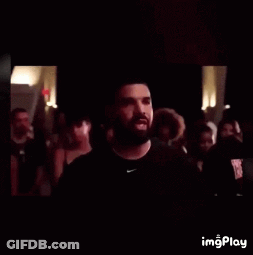 A Man With A Beard Wearing A Black Nike Shirt Stands In Front Of A Crowd Of People GIF