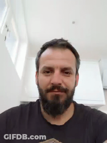 A Man With A Beard Wearing A Black Shirt Is Smiling And Looking At The Camera . GIF