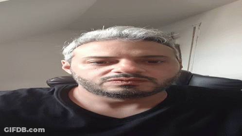 A Man With A Beard Wearing A Black Shirt Looks Down At The Camera GIF