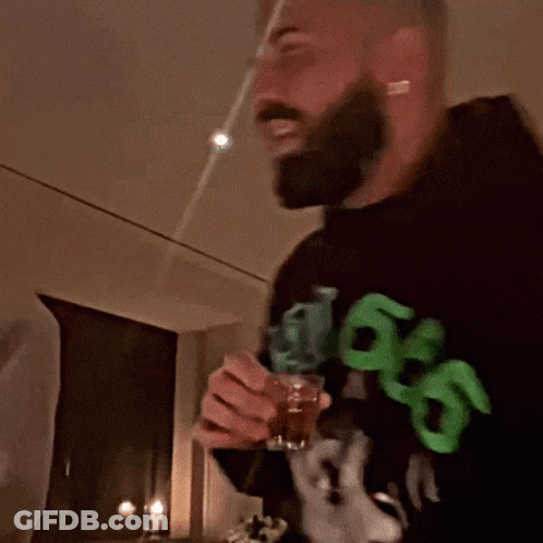 A Man With A Beard Wearing A Black Sweatshirt With Green Letters That Says 99 On It GIF
