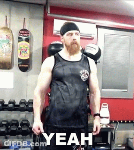 A Man With A Beard Wearing A Black Tank Top Is Standing In A Gym With The Word Yeah Written On The Bottom GIF