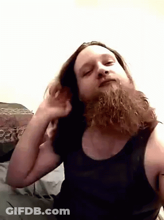 A Man With A Beard Wearing A Black Tank Top Looks At The Camera GIF