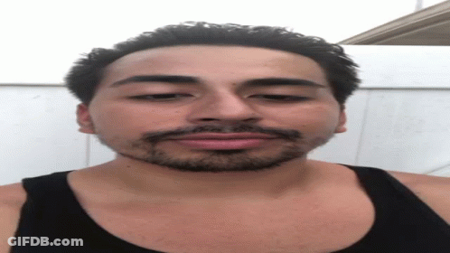 A Man With A Beard Wearing A Black Tank Top Looks At The Camera GIF