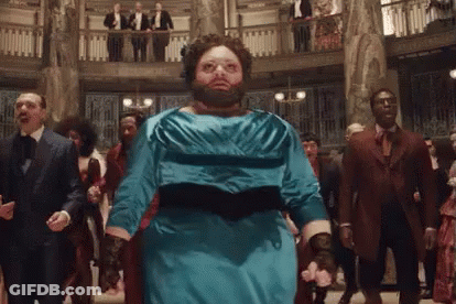 A Man With A Beard Wearing A Blue Dress Is Dancing In A Room With Other People . GIF