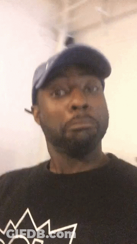 A Man With A Beard Wearing A Blue Hat And A Black Shirt With A Crown On It . GIF