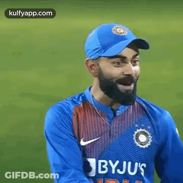 A Man With A Beard Wearing A Blue Hat And A Blue Shirt Is Standing On A Field . GIF