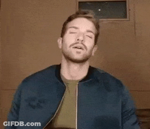 A Man With A Beard Wearing A Blue Jacket And A Green Shirt Is Making A Funny Face . GIF