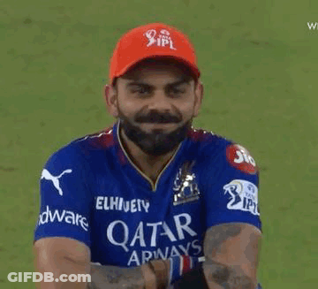 A Man With A Beard Wearing A Blue Shirt And A Red Hat Is Holding A Cricket Ball . GIF