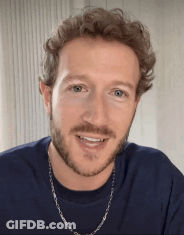 A Man With A Beard Wearing A Blue Shirt And A Silver Chain Around His Neck GIF
