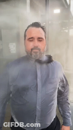 A Man With A Beard Wearing A Blue Shirt And Tie Is Standing In A Foggy Room GIF