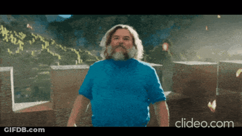 A Man With A Beard Wearing A Blue Shirt Is Standing In Front Of A Pile Of Cardboard Boxes GIF