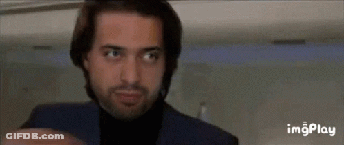 A Man With A Beard Wearing A Blue Suit And Black Turtleneck Is Looking Up . GIF