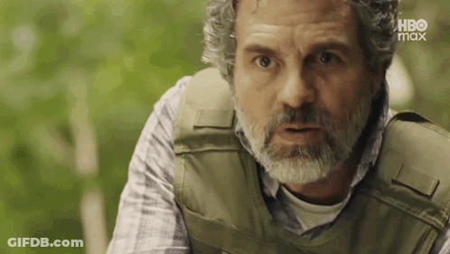 A Man With A Beard Wearing A Bullet Proof Vest Is Looking At The Camera . GIF