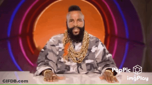 A Man With A Beard Wearing A Camouflage Jacket And Gold Chains Is Sitting At A Table With His Hands On The Table GIF