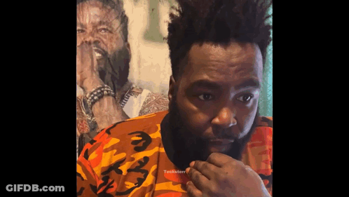 A Man With A Beard Wearing A Camouflage Shirt Looks At The Camera GIF