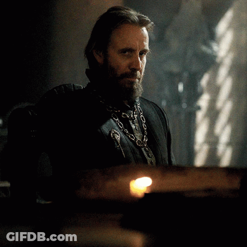 A Man With A Beard Wearing A Chain Around His Neck Looks At The Camera GIF