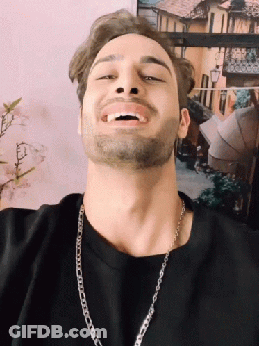 A Man With A Beard Wearing A Chain Around His Neck Smiles GIF