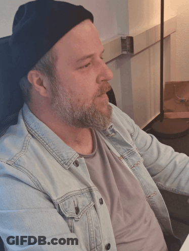 A Man With A Beard Wearing A Denim Jacket And A Black Beanie GIF
