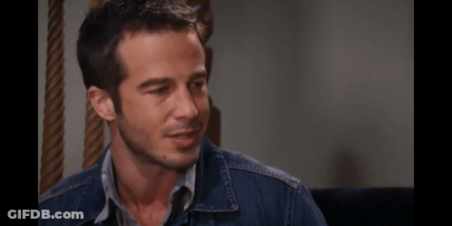A Man With A Beard Wearing A Denim Jacket Looks Down At Something GIF