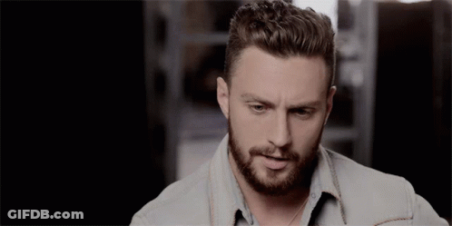 A Man With A Beard Wearing A Denim Shirt Looks At The Camera GIF