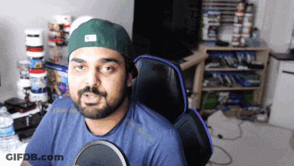A Man With A Beard Wearing A Green Hat Is Sitting In A Chair GIF