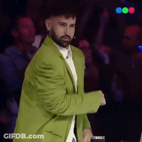 A Man With A Beard Wearing A Green Jacket Stands In Front Of A Crowd GIF