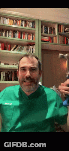 A Man With A Beard Wearing A Green Scrub Top With The Name Ricky On The Front Pocket GIF