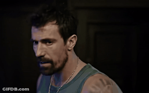 A Man With A Beard Wearing A Green Tank Top Looks At The Camera GIF