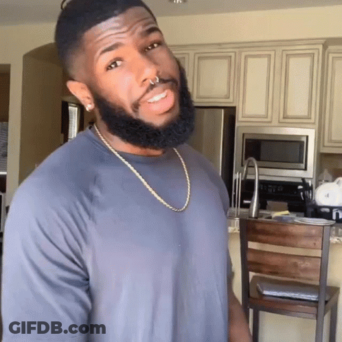 A Man With A Beard Wearing A Grey Shirt And A Gold Chain GIF