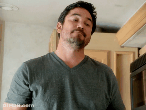A Man With A Beard Wearing A Grey Shirt Looks At The Camera GIF