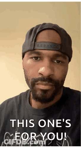 A Man With A Beard Wearing A Hat And A Black Shirt Says " This One 'S For You " GIF