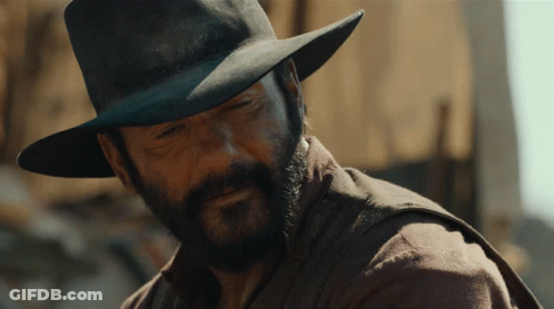 A Man With A Beard Wearing A Hat And A Brown Shirt GIF