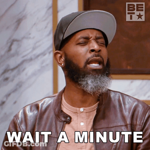 A Man With A Beard Wearing A Hat And A Leather Jacket Says " Wait A Minute " GIF