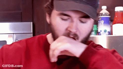 A Man With A Beard Wearing A Hat And A Red Shirt Eating GIF